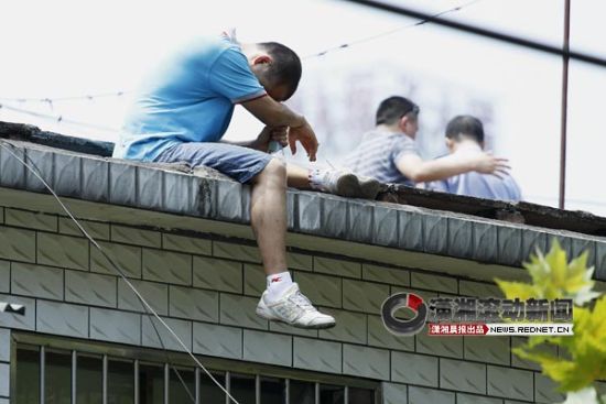 (今日上午11时许，一男子坐在长沙浏正街巷子一栋4层楼的房顶，他的孩子因为注射疫苗出现了问题。图/潇湘晨报滚动新闻实习生 杨旭)
