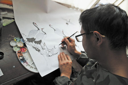 李盛明在画他擅长的工笔动物画，他笔下的仙鹤笔法细腻，栩栩如生。